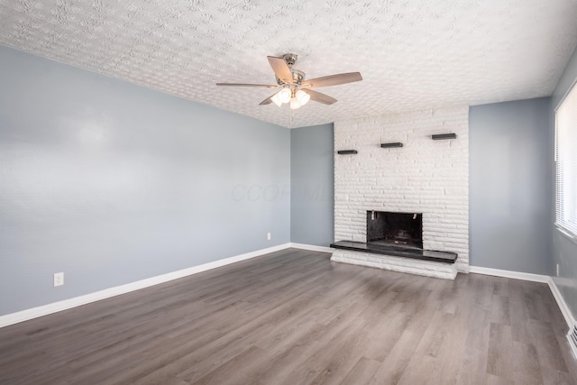 unfurnished living room featuring dark wood-type flooring, ceiling fan, a fireplace, and a textured ceiling