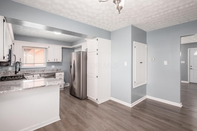 kitchen featuring hardwood / wood-style floors, stainless steel appliances, light stone countertops, a textured ceiling, and white cabinets