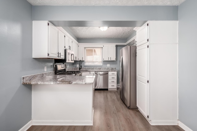 kitchen with white cabinetry, stainless steel appliances, kitchen peninsula, and a textured ceiling