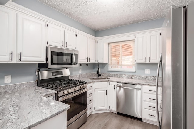 kitchen featuring white cabinetry, sink, light hardwood / wood-style floors, stainless steel appliances, and a textured ceiling