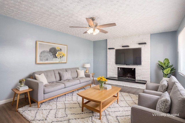 living room featuring hardwood / wood-style flooring, ceiling fan, a fireplace, and a textured ceiling