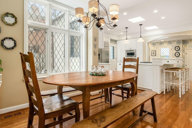 dining area featuring a notable chandelier, light hardwood / wood-style flooring, crown molding, and a skylight