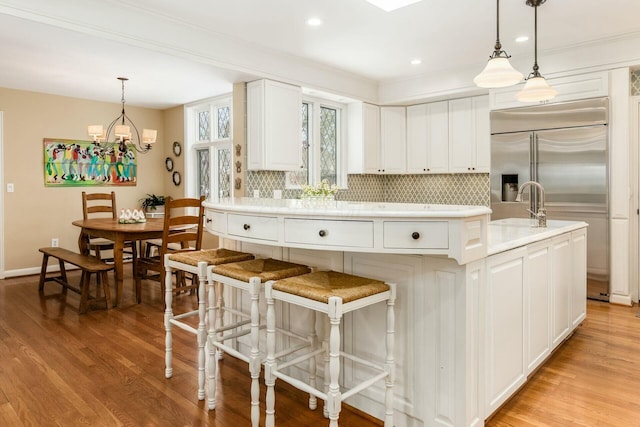 kitchen with light hardwood / wood-style flooring, an island with sink, white cabinets, decorative backsplash, and pendant lighting