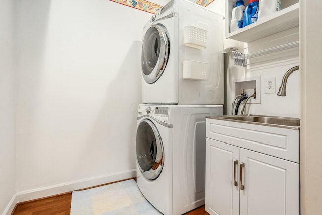 laundry area featuring sink, stacked washer / drying machine, cabinets, and hardwood / wood-style floors