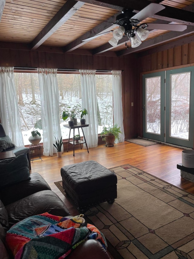 living room with beamed ceiling, plenty of natural light, light hardwood / wood-style floors, and wood walls