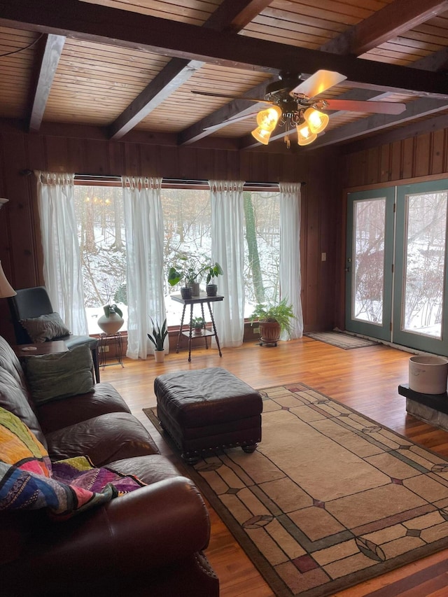 living room featuring ceiling fan, beam ceiling, wood walls, wooden ceiling, and light wood-type flooring