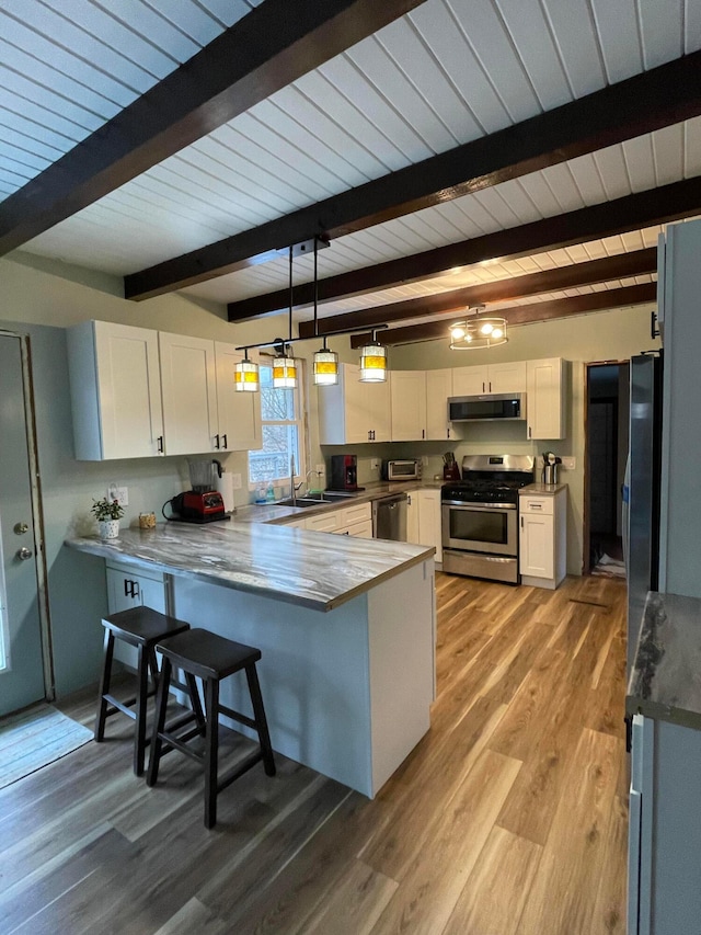 kitchen featuring appliances with stainless steel finishes, decorative light fixtures, white cabinetry, a breakfast bar area, and kitchen peninsula