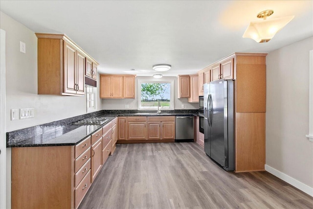 kitchen with light brown cabinetry, appliances with stainless steel finishes, a sink, baseboards, and light wood-type flooring