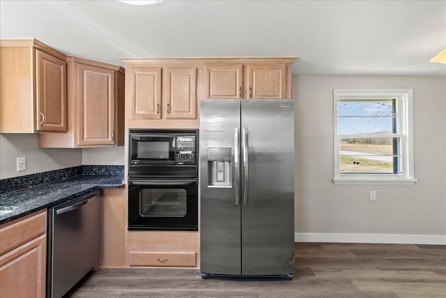 kitchen featuring light brown cabinetry, wood finished floors, baseboards, black appliances, and dark stone counters