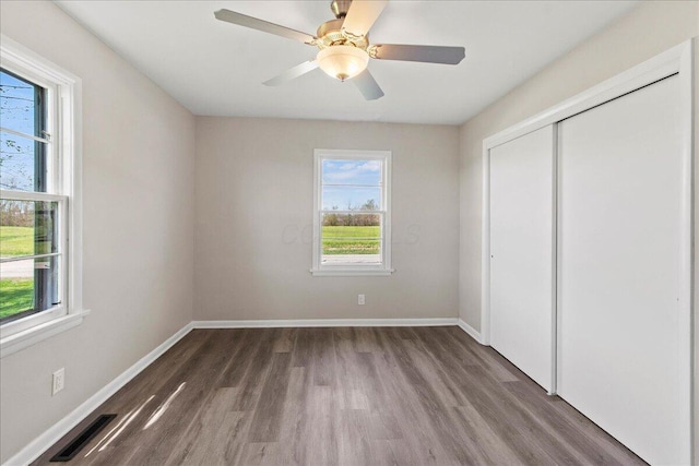 unfurnished bedroom with baseboards, a closet, wood finished floors, and visible vents