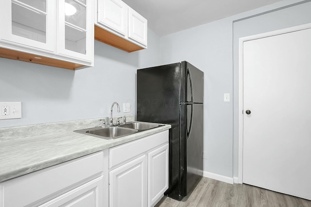 kitchen featuring black refrigerator, sink, white cabinets, and light wood-type flooring