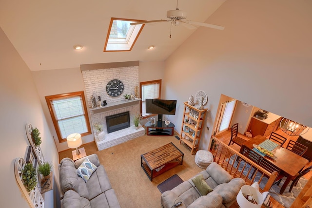 carpeted living room with ceiling fan, a fireplace, a skylight, and high vaulted ceiling