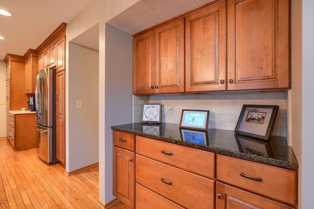 kitchen with dark stone countertops, backsplash, stainless steel refrigerator, and light hardwood / wood-style floors