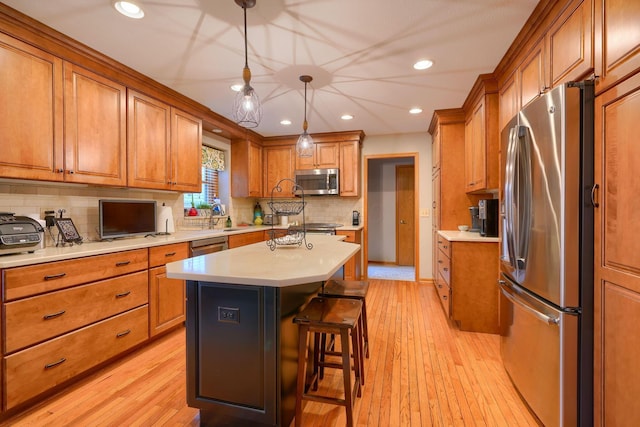 kitchen with a breakfast bar area, hanging light fixtures, a center island, stainless steel appliances, and light hardwood / wood-style flooring