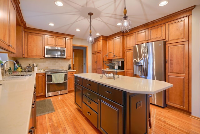 kitchen with decorative light fixtures, sink, a center island, stainless steel appliances, and light hardwood / wood-style flooring