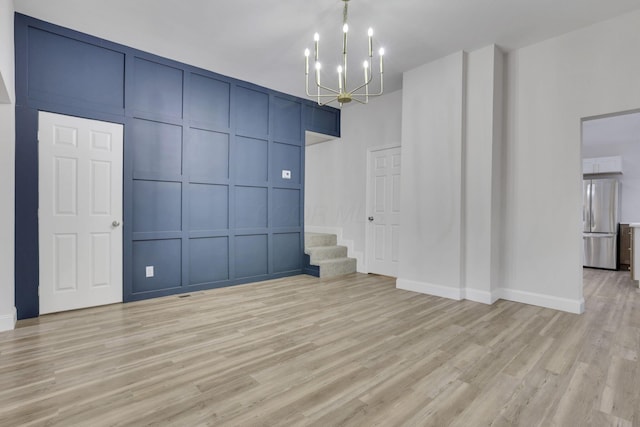 spare room featuring a notable chandelier and light hardwood / wood-style flooring