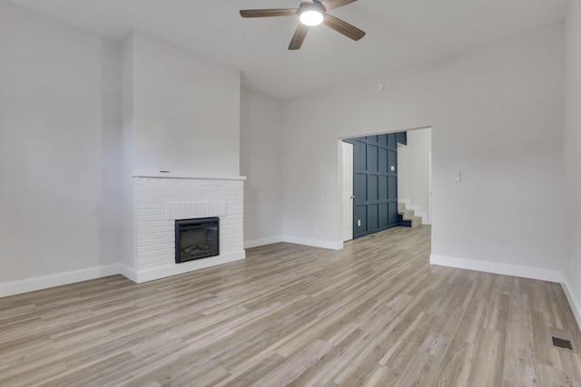 unfurnished living room with a brick fireplace, ceiling fan, and light hardwood / wood-style flooring