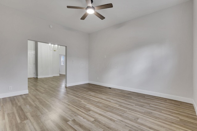 empty room with ceiling fan with notable chandelier and light wood-type flooring