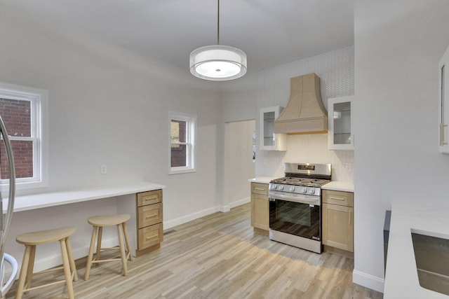 kitchen with premium range hood, light brown cabinetry, light hardwood / wood-style flooring, stainless steel range with gas cooktop, and decorative backsplash