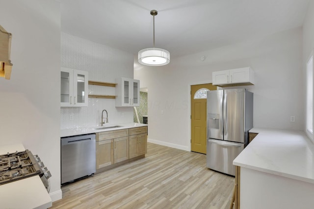 kitchen with sink, appliances with stainless steel finishes, white cabinetry, decorative light fixtures, and light wood-type flooring