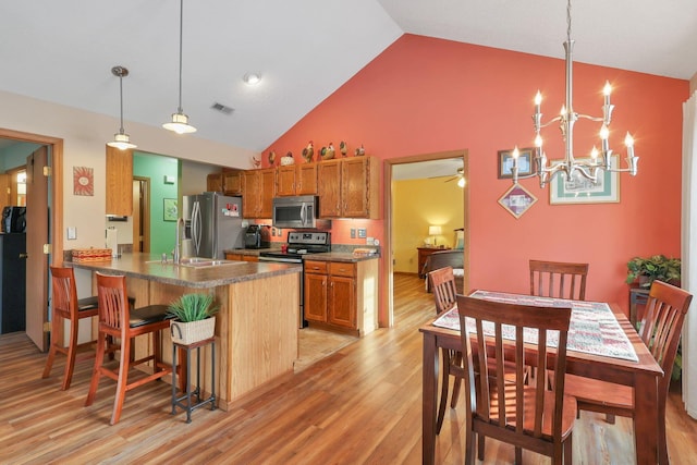 kitchen with a breakfast bar area, light wood-type flooring, appliances with stainless steel finishes, kitchen peninsula, and pendant lighting