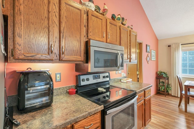 kitchen with stainless steel appliances, vaulted ceiling, light hardwood / wood-style flooring, and a textured ceiling