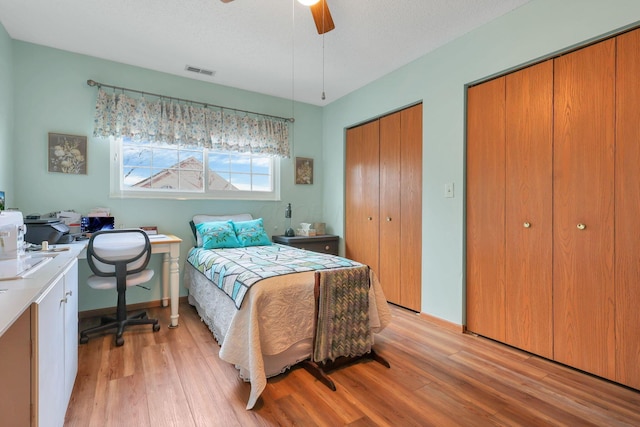 bedroom with ceiling fan, a textured ceiling, light hardwood / wood-style flooring, and two closets