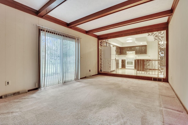 unfurnished living room with light carpet, beam ceiling, and wooden walls