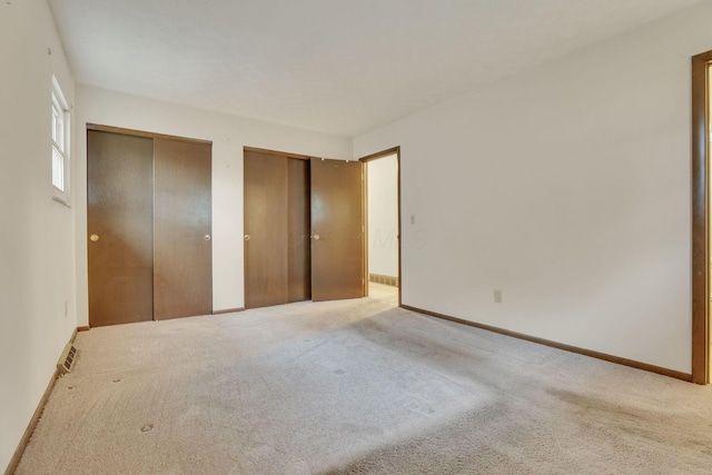 unfurnished bedroom featuring multiple closets and light carpet