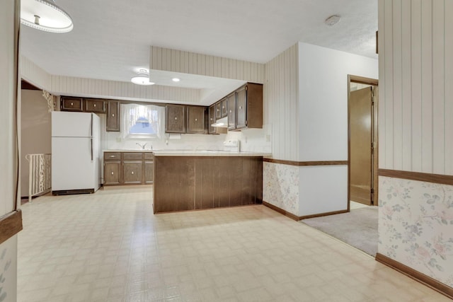 kitchen featuring dark brown cabinets, kitchen peninsula, and white refrigerator