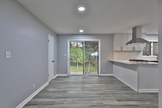 kitchen with island range hood, white cabinets, stainless steel gas stovetop, light hardwood / wood-style floors, and backsplash