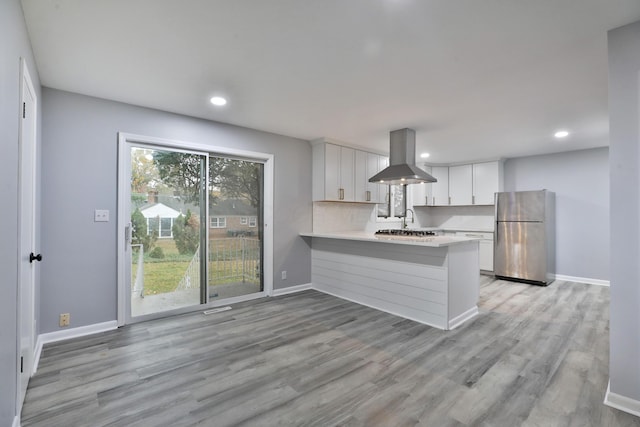 kitchen featuring stainless steel fridge, kitchen peninsula, island exhaust hood, light hardwood / wood-style floors, and white cabinets