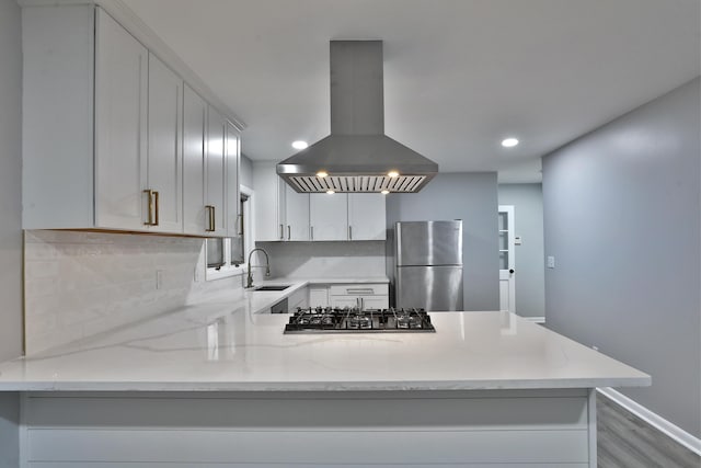 kitchen with appliances with stainless steel finishes, island range hood, sink, decorative backsplash, and light stone countertops