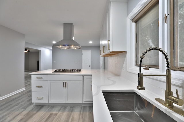 kitchen featuring stainless steel gas stovetop, white cabinetry, sink, island exhaust hood, and light hardwood / wood-style flooring