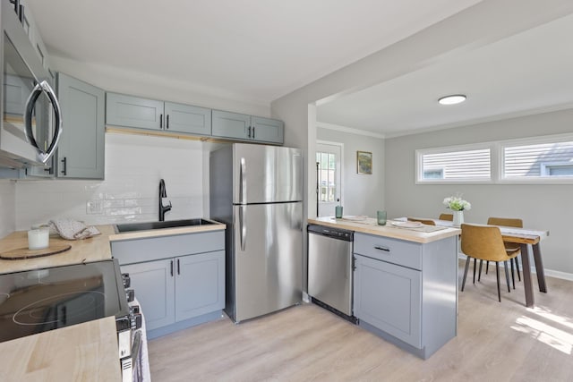 kitchen with sink, crown molding, light hardwood / wood-style flooring, stainless steel appliances, and decorative backsplash