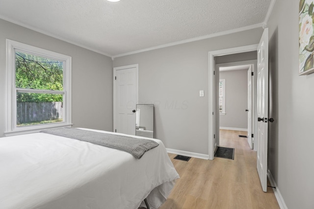 bedroom featuring crown molding, multiple windows, light hardwood / wood-style flooring, and a textured ceiling