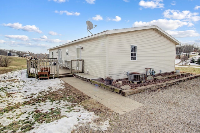 snow covered rear of property featuring central AC unit and a deck