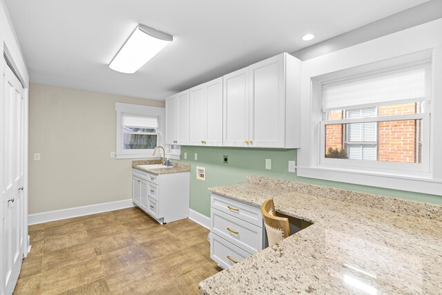 kitchen with built in desk, light stone countertops, sink, and white cabinets