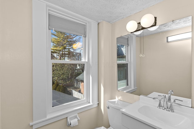 bathroom with a healthy amount of sunlight, toilet, a textured ceiling, and vanity