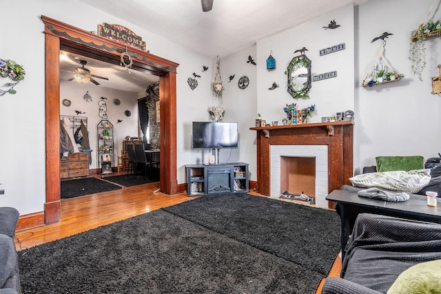 living room with hardwood / wood-style floors, ceiling fan, and a brick fireplace