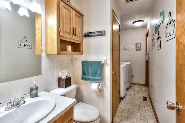 bathroom with vanity, separate washer and dryer, tile walls, and toilet