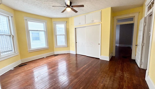 unfurnished bedroom featuring multiple windows, a closet, dark hardwood / wood-style floors, and a textured ceiling