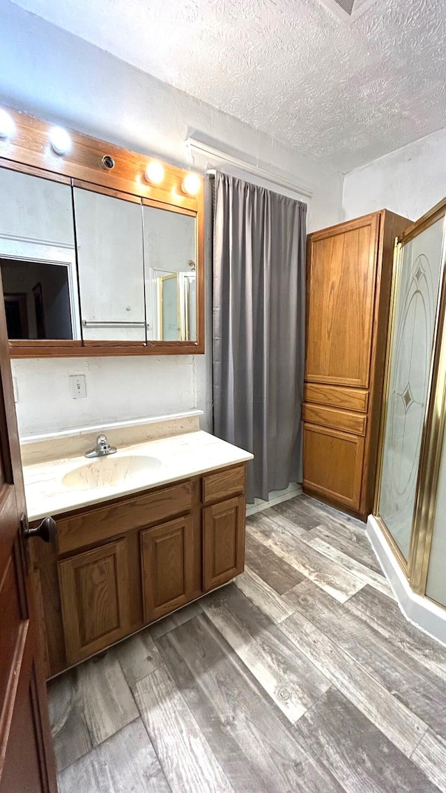 bathroom with vanity, an enclosed shower, wood-type flooring, and a textured ceiling