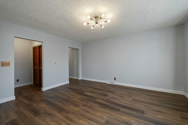 empty room with an inviting chandelier, a textured ceiling, and dark hardwood / wood-style flooring