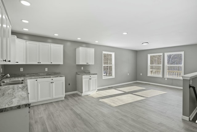 kitchen featuring white cabinetry, light stone countertops, sink, and light hardwood / wood-style flooring