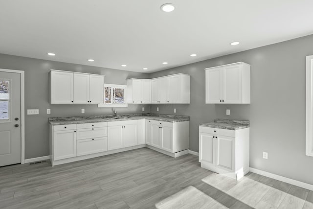 kitchen with white cabinetry, light hardwood / wood-style floors, sink, and light stone counters