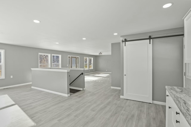 kitchen with light stone counters, a barn door, white cabinets, and light wood-type flooring