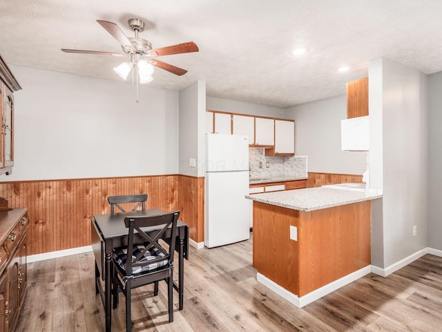 kitchen featuring white refrigerator, white cabinets, wooden walls, and light wood-type flooring