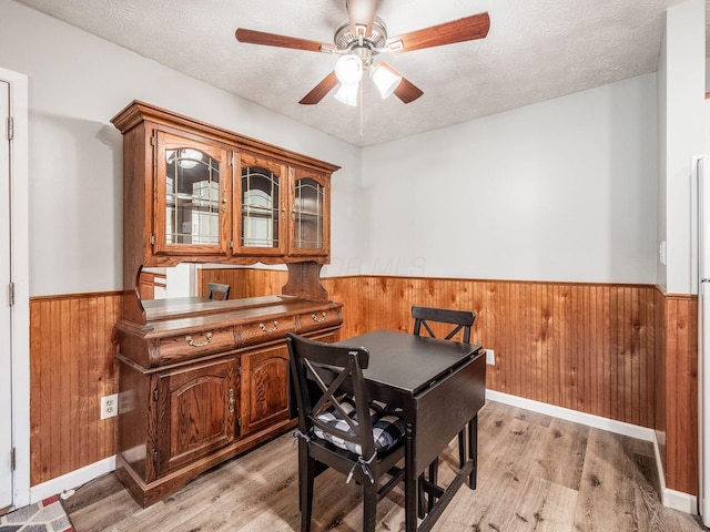 dining room featuring ceiling fan, light wood-type flooring, a textured ceiling, and wooden walls