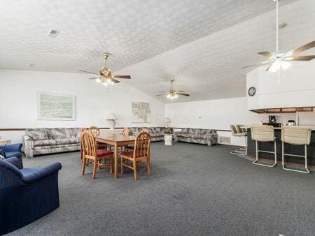 carpeted dining area featuring ceiling fan, vaulted ceiling, and a textured ceiling